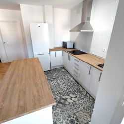 Cocina reformada con muebles blancos y madera de tono claro y suelo cerámico con dibujo geométrico