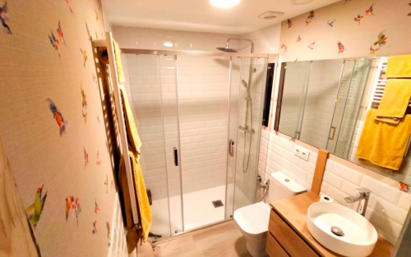 Baño reformado con muebles de madera en tono claro y pared empapelada con motivo de pájaros