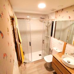 Baño reformado con muebles de madera en tono claro y pared empapelada con motivo de pájaros